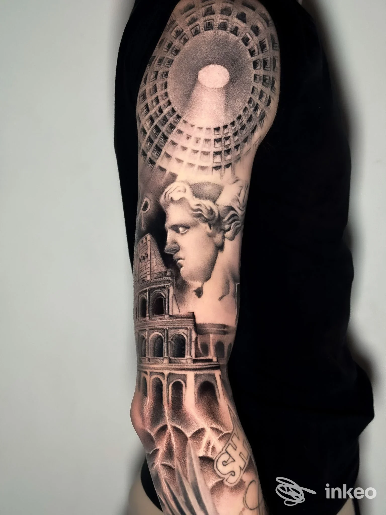 Manica tatuata realistico in bianco e nero con volto scultoreo e architettura, foto inviata da Sangue Blu Tattoo Shop, Roma.