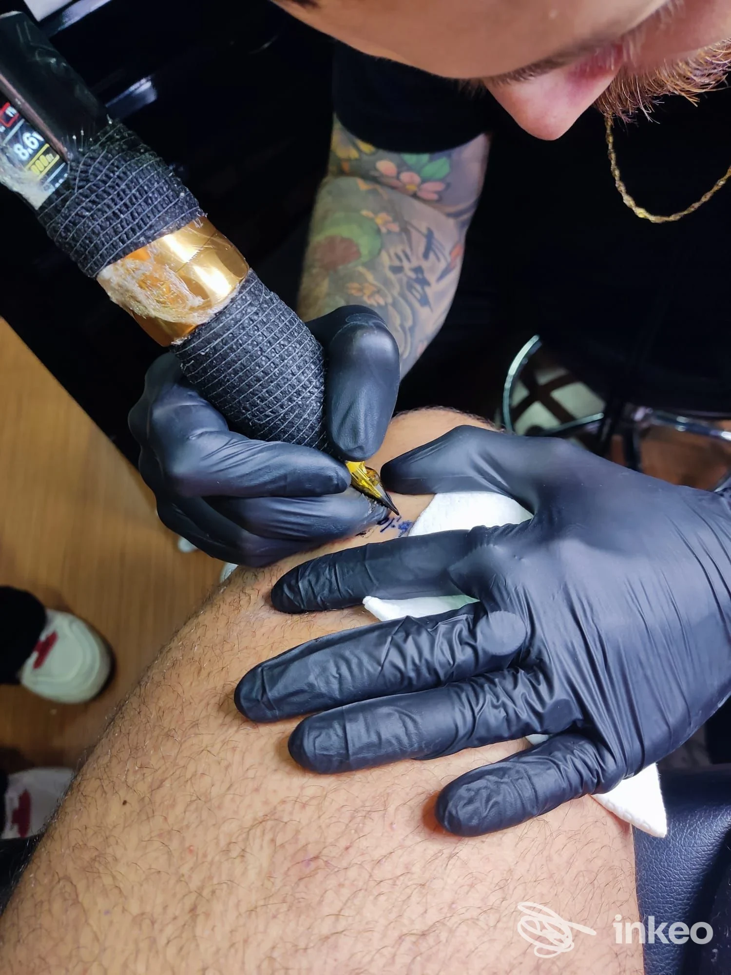 Tatuatore al lavoro sulla coscia, macchina e mani con guanti neri; Santipeccatori Tatuaggi, Roma.
