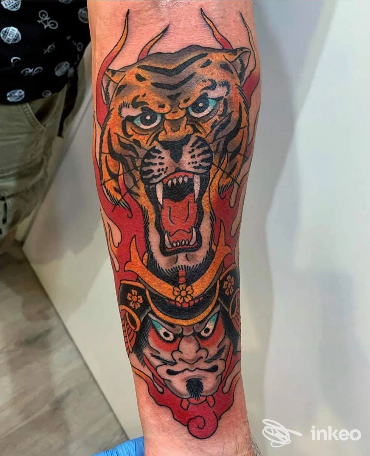 Tatuaggio su avambraccio con testa di tigre ruggente sopra una maschera e fiamme, lavoro fotografato da Sorry Mama Tattoo Studio, Pomezia.