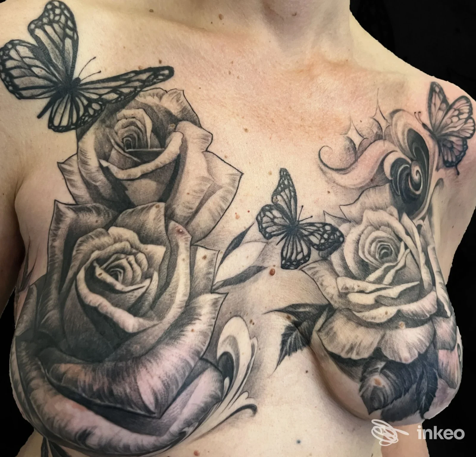 Grande tatuaggio floreale in bianco e nero su petto e seni, con rose e farfalle. Self Made Tattoo Shop, San Giovanni Incarico.