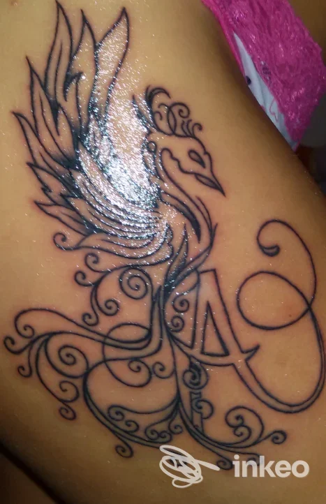 Tatuaggio nero ornamentale a forma di uccello con lettera 'A' sul fianco, immagine fornita da T.P. Tracce Permanenti Di Palumbo Alessio, Tivoli Terme.