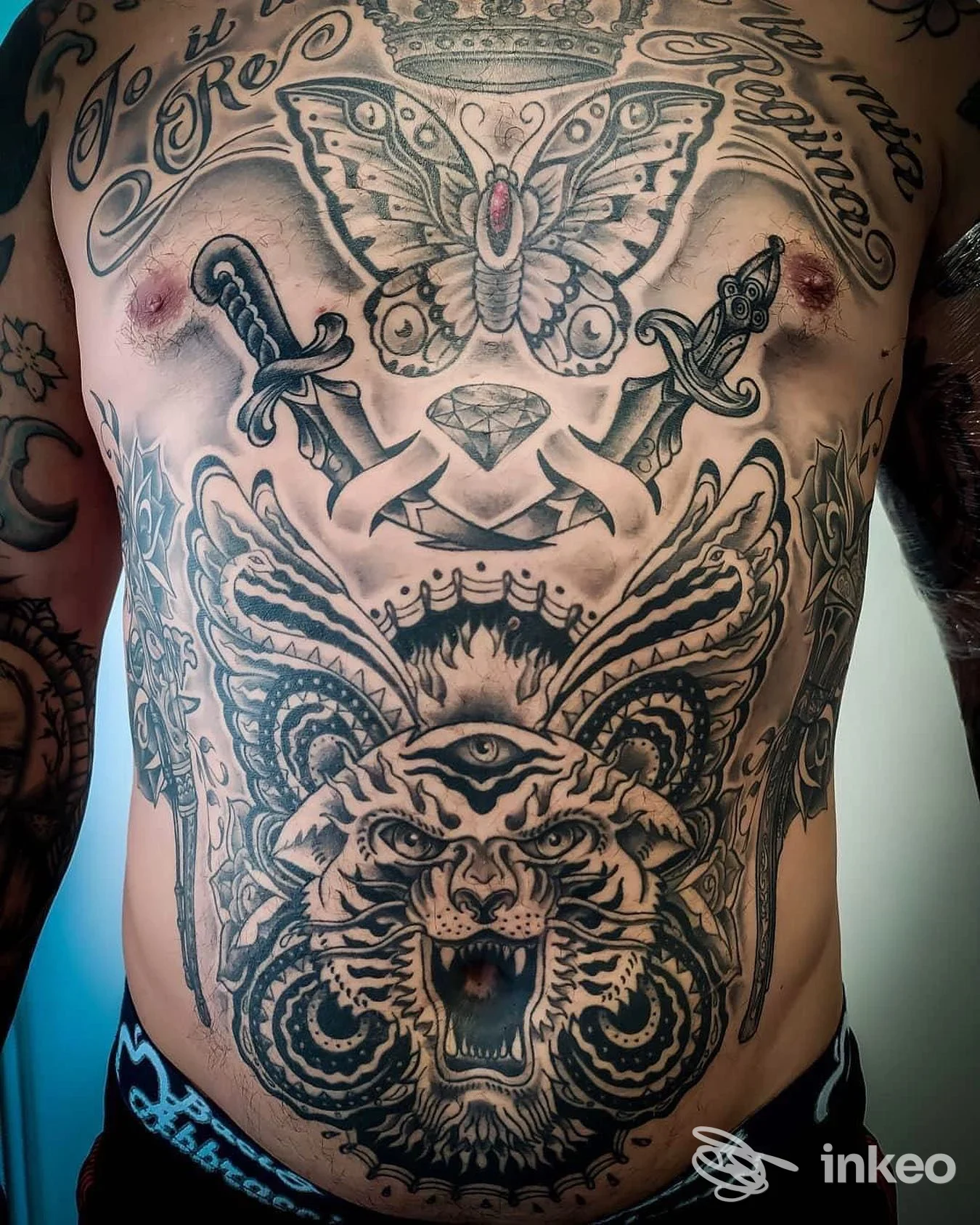 Tatuaggi in bianco e nero su petto e addome, tra cui una farfalla centrale e una grande testa di felino; Stigma Tattoo, Roma.