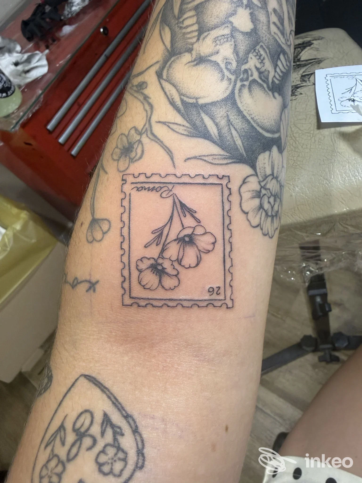 Primo piano di un tatuaggio a inchiostro nero con fiori incorniciati come un francobollo sull'avambraccio; Swan Song Tattoo, Roma.