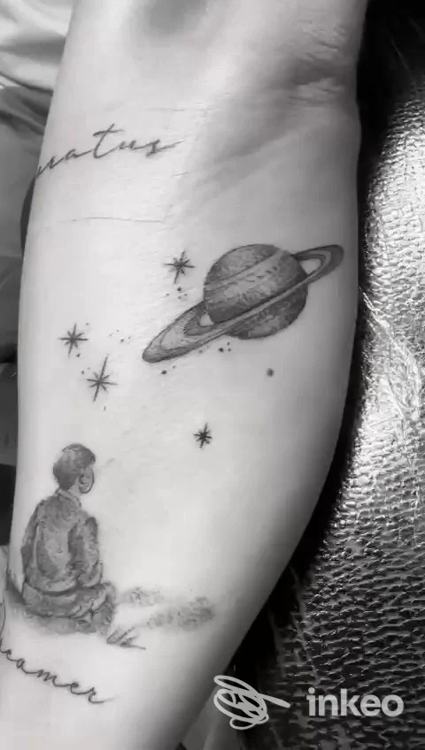 Primo piano di un avambraccio tatuato con pianeta, stelle e figura seduta — Swan Song Tattoo, Trastevere, Roma.