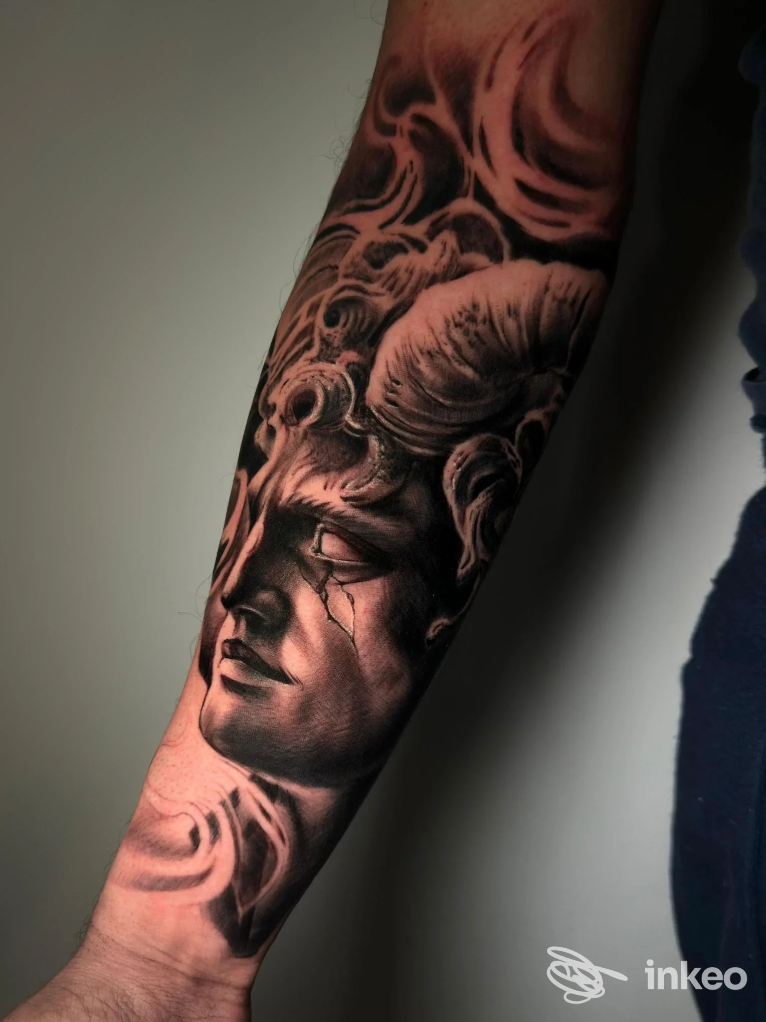 Primo piano di un tatuaggio sull'avambraccio raffigurante un volto scultoreo con corna, realizzato da TM TATTOO a Roma.