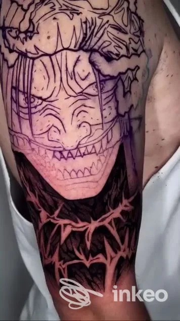 Parte superiore del braccio con tatuaggio in corso: contorni di volto e linee del disegno in fase di realizzazione, con area d'ombra nera; studio Neo Anime Tattoo Studio, Meda.
