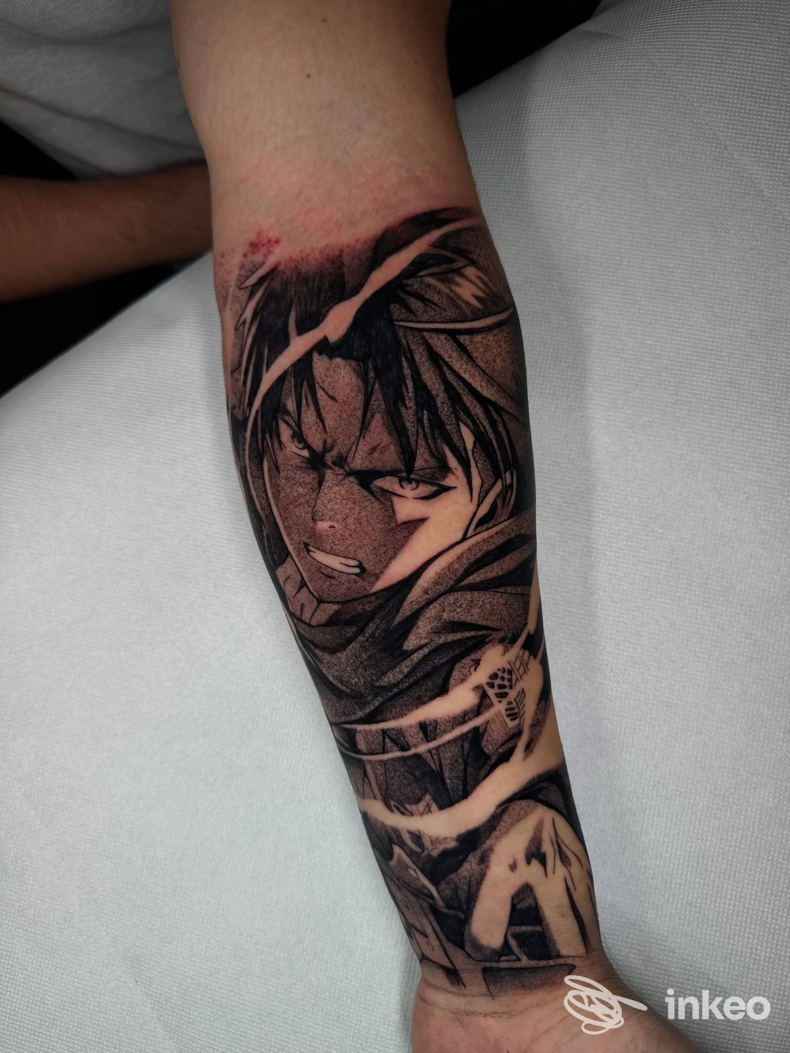 Braccio di una persona con tatuaggio in stile manga/anime, ritratti scuro di un personaggio con linee nette e tonalità nere, sull'avambraccio sinistro.