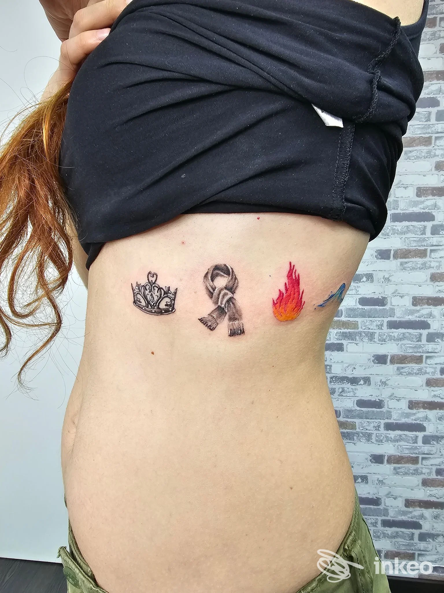 Foto del lato torace con quattro piccoli tatuaggi realizzati da The Painter Tattoo ad Agosta, corona, nastro, fiamma e piccolo simbolo colorato.