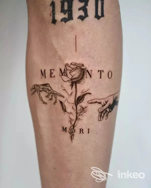 Tatuaggio su gamba con rosa centrale, mani laterali e le parole 'MEMENTO MORI' — immagine fornita da TATTOO49 Roma.