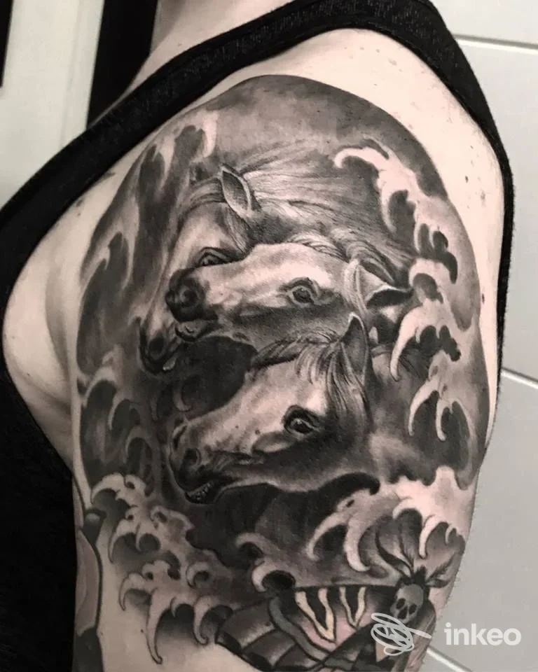 Tatuaggio realistico in bianco e nero con tre teste di cavallo e onde sul braccio superiore, foto fornita da Underdog Tattoo Roma, Roma.
