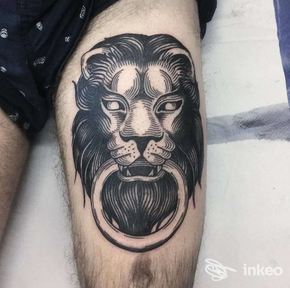 Tatuaggio nero a inchiostro su coscia con testa di leone stilizzata e anello; foto fornita da Underdog Tattoo Roma, Roma.
