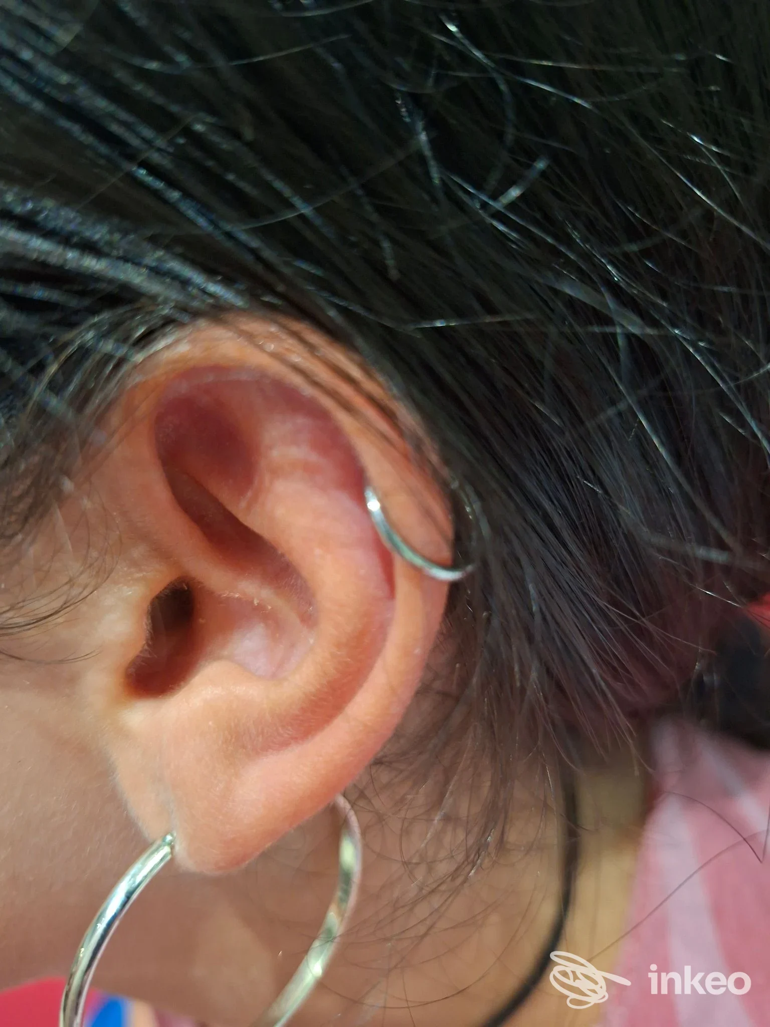 Primo piano dell'orecchio con due piercing a cerchio eleganti; immagine fornita da The New Family Tattoo, Roma.