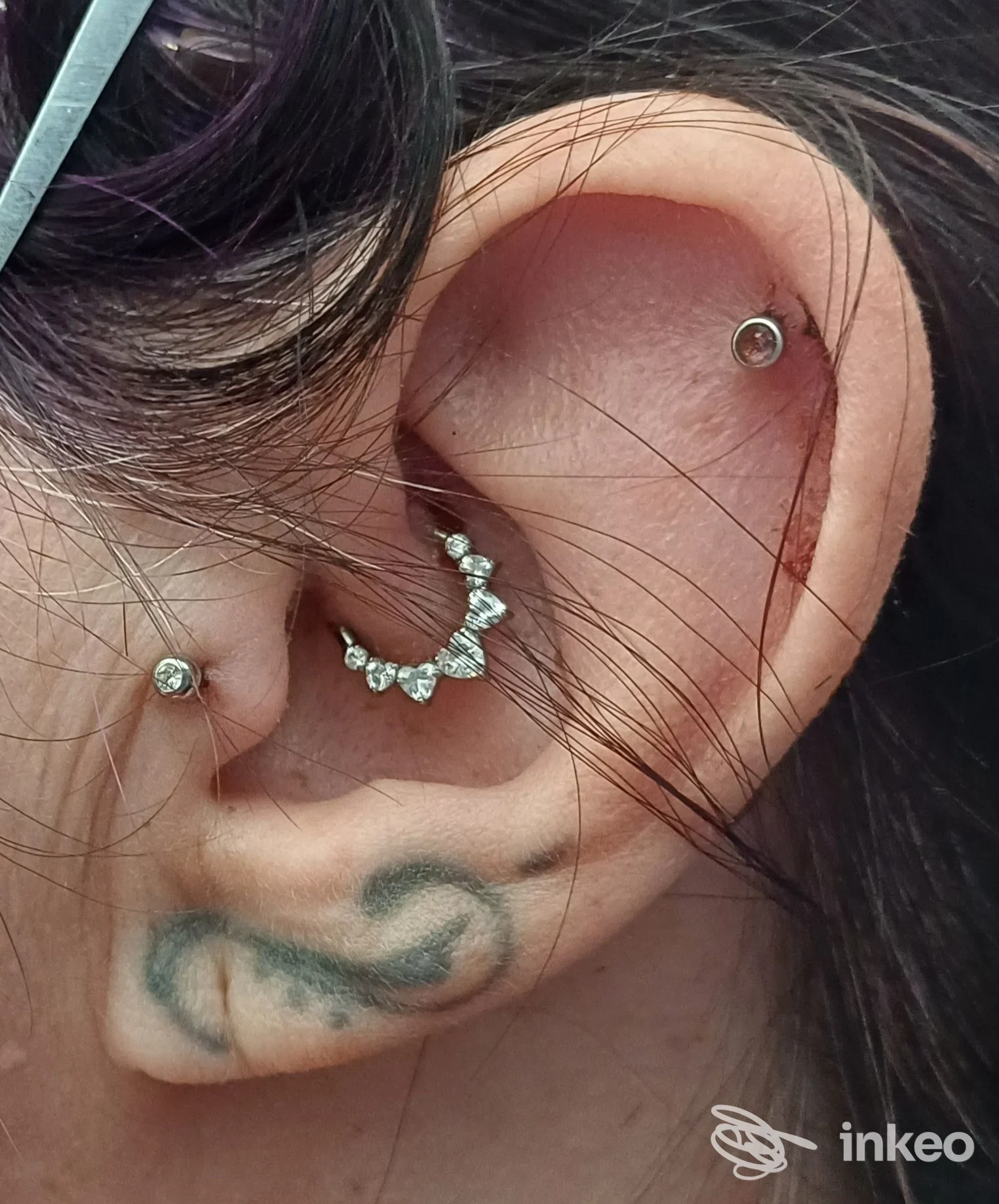 Primo piano di un orecchio con più piercing e un piccolo tatuaggio sul lobo. Immagine fornita da The New Family Tattoo, Roma.