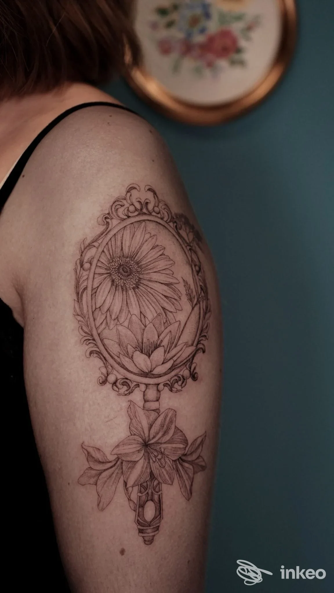 Tatuaggio floreale in nero sul braccio superiore: cornice ovale con margherita e giglio, foto di Violet tattoo studio, Roma.
