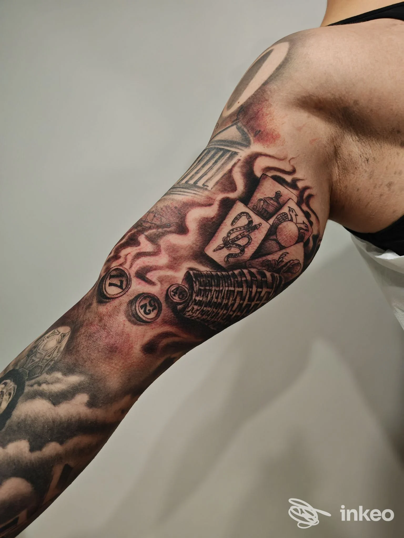 Manica tatuata su braccio con carte, monete e colonna, fotografia del lavoro eseguito da Xaba Tattoo Studio a Fondi.