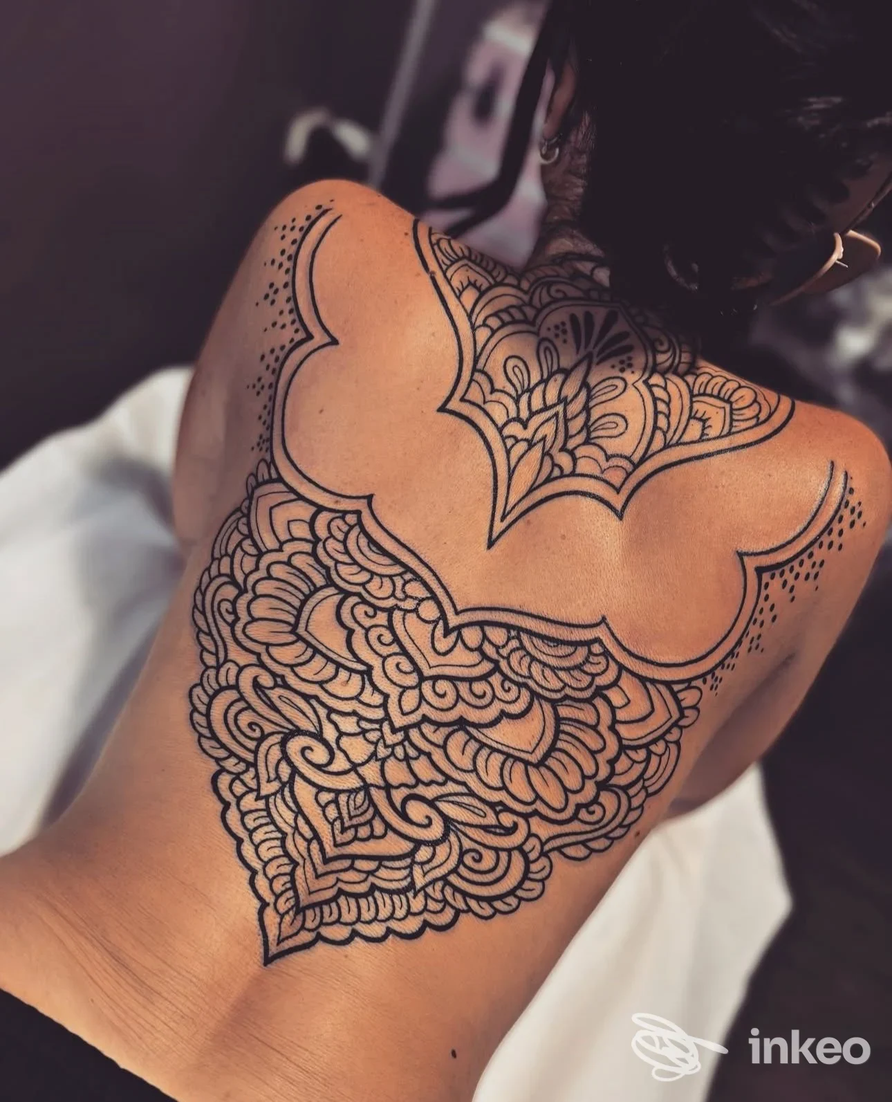 Tattoo grande e dettagliato sulla schiena, con motivi geometrici e ornati, senza volto visibile, scatto in orientamento laterale su schiena nuda.