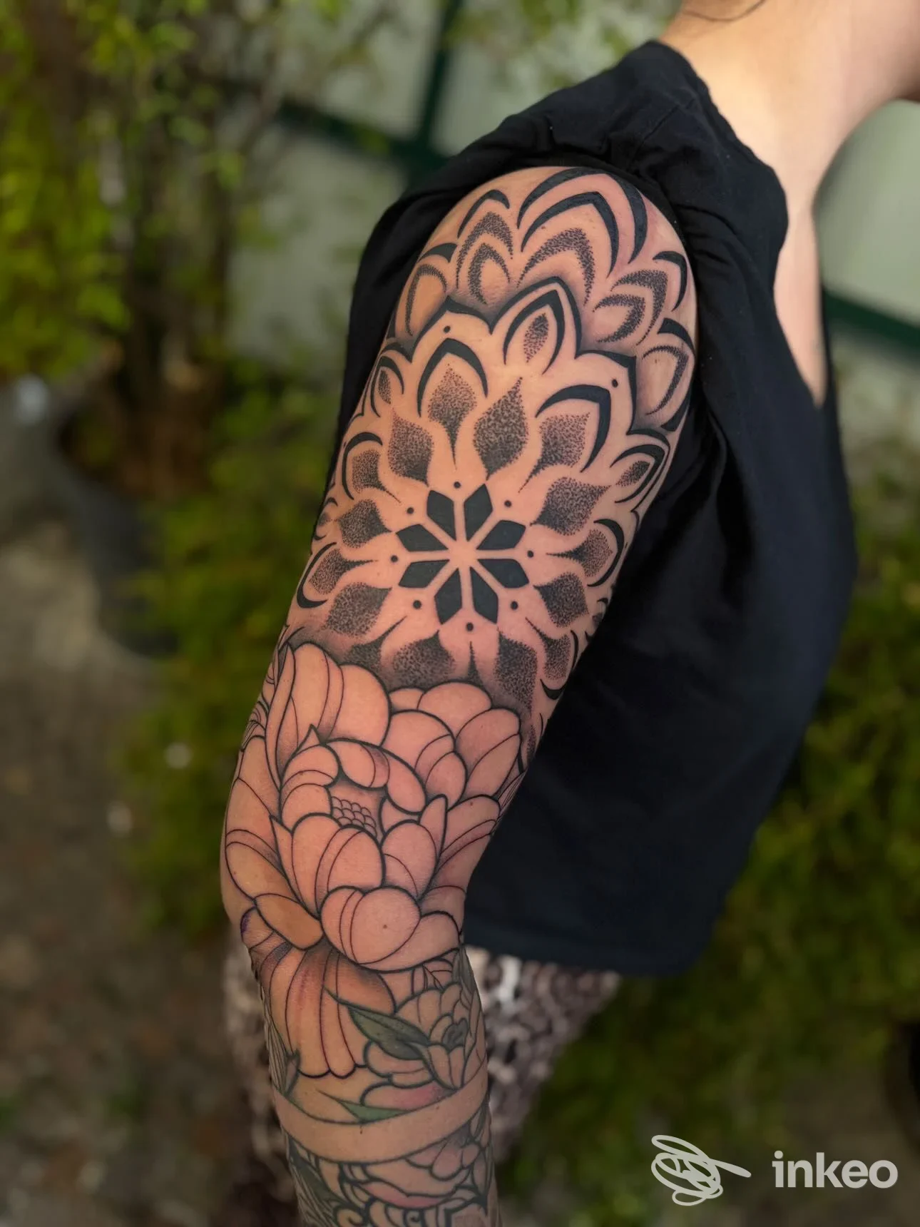 Tattoo geometrico-floreale visibile sulla parte superiore del braccio di una persona, senza volto visibile e senza testo o watermark.