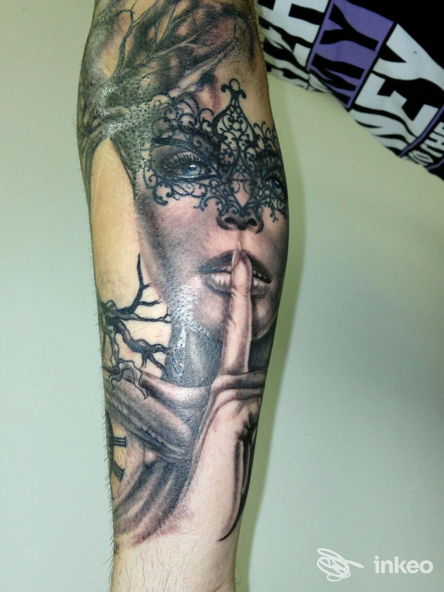 Tatuaggio realistico su avambraccio raffigurante volto con maschera e dito sulle labbra - Ars Tattoo Studio, Roma.