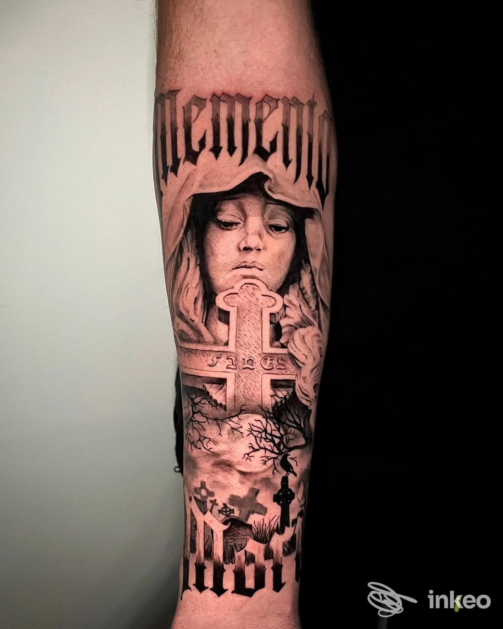 Avambraccio con tatuaggio black-and-grey raffigurante volto incappucciato, croce e lettering, realizzato da Black Blood tattoo a Anguillara Sabazia.