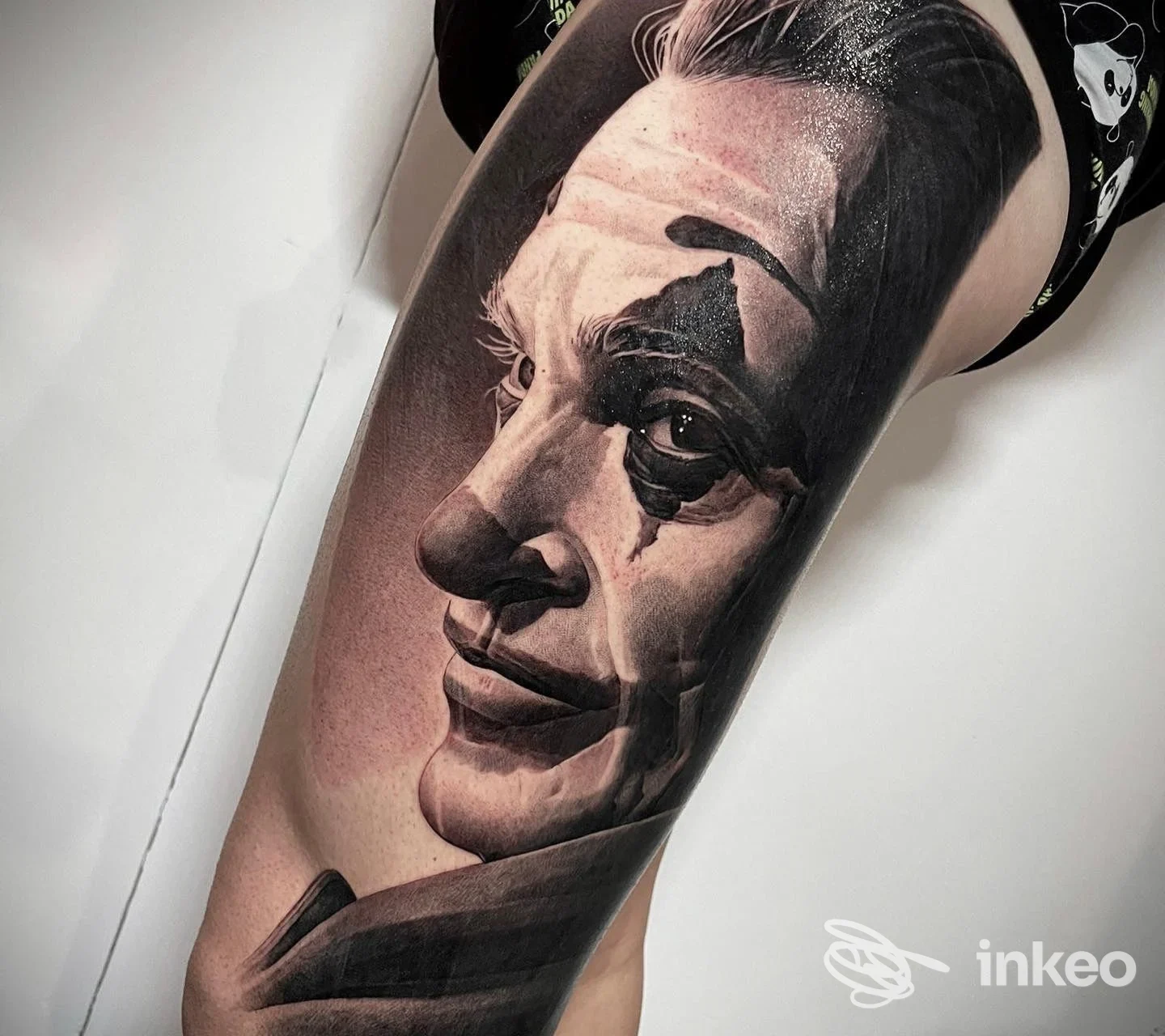 Grande tatuaggio realistico in bianco e nero raffigurante un volto stile clown sulla coscia, foto fornita da Cromo Tattoo Studio, Roma.