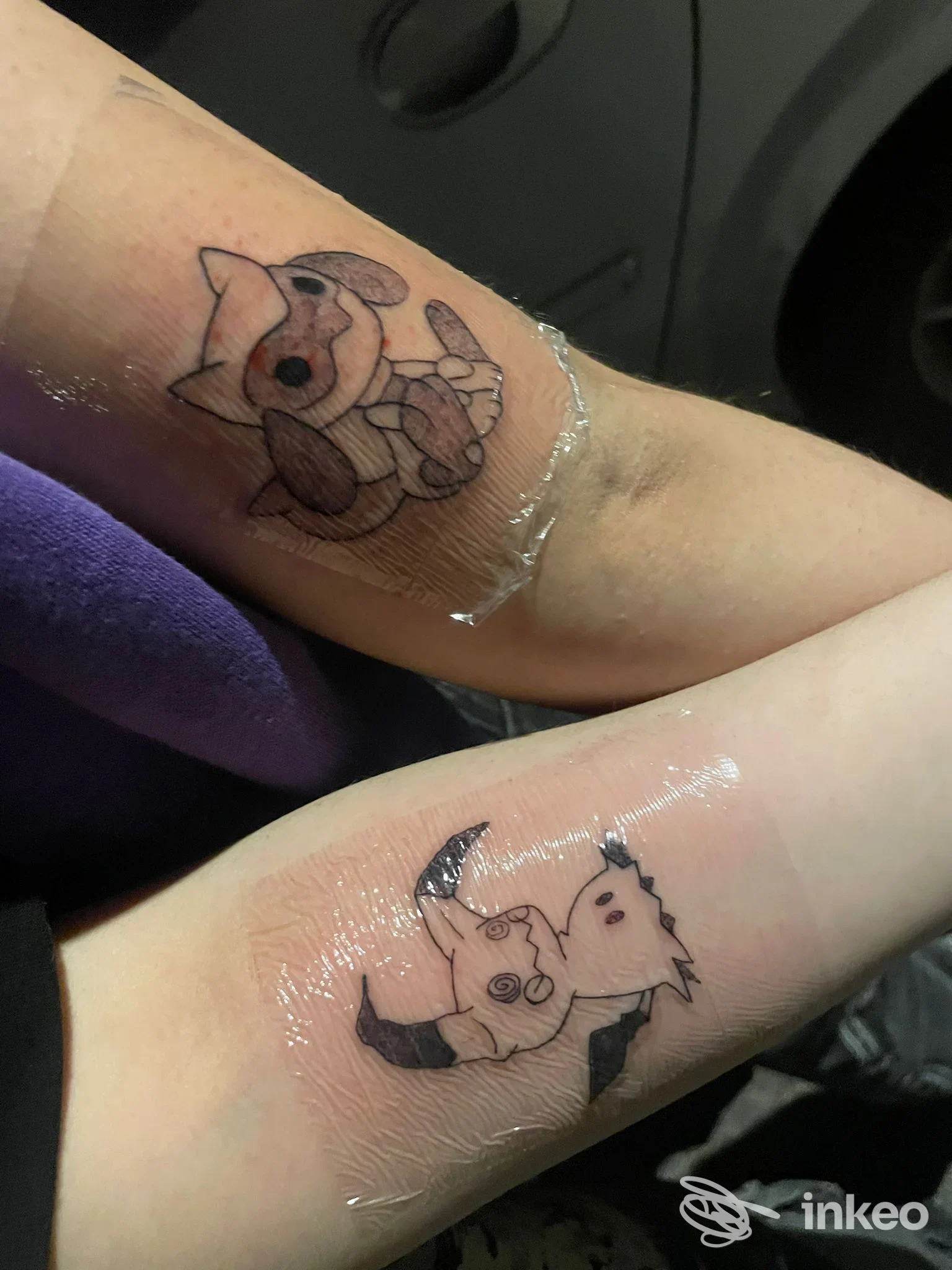 Due tatuaggi freschi in stile cartoon sugli avambracci con pellicola protettiva. Centipede Tattoo Studio, Tivoli.