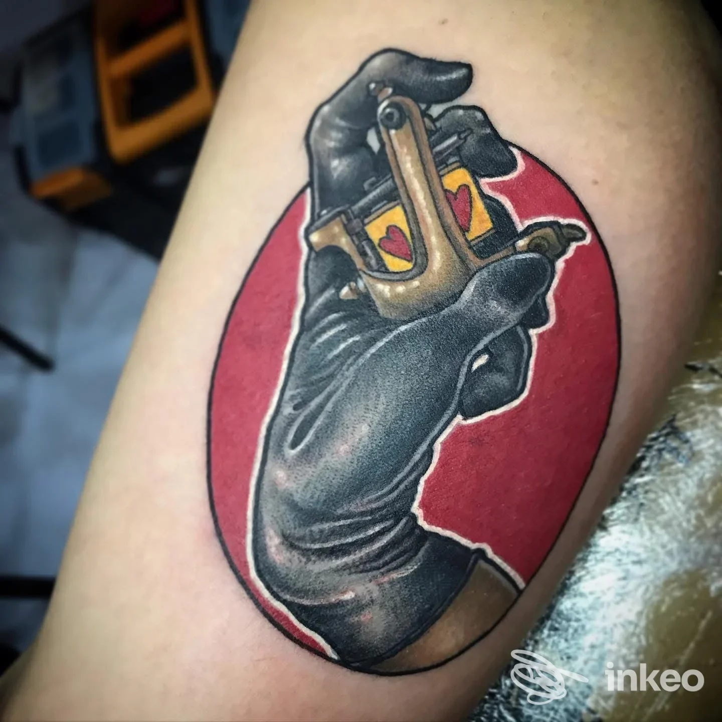 Tatuaggio su braccio: mano guantata nera con macchinetta, ovale rosso. InkFactory Tattoo, Roma.