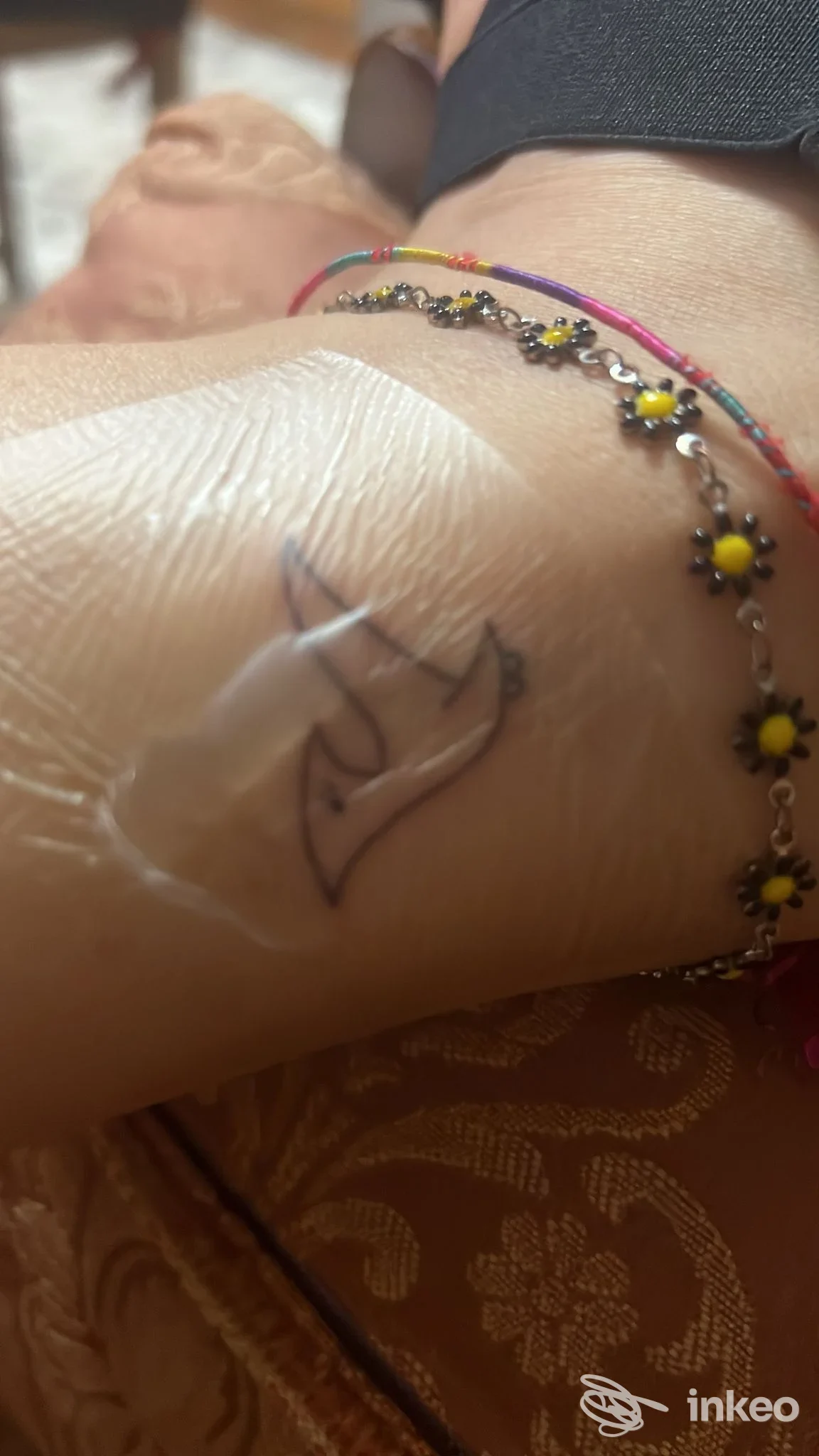 Primo piano di un piccolo tatuaggio lineare nero sul polso coperto da pellicola protettiva, con braccialetti; Jade_tattoo_ & piercing studio, Fiumicino.