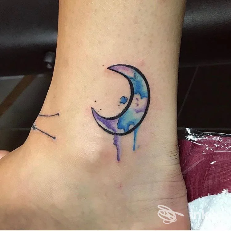 Piccolo tatuaggio a mezzaluna in stile acquerello sulla caviglia, con sfumature blu e viola, realizzato da LaSux Tattoo a Roma.