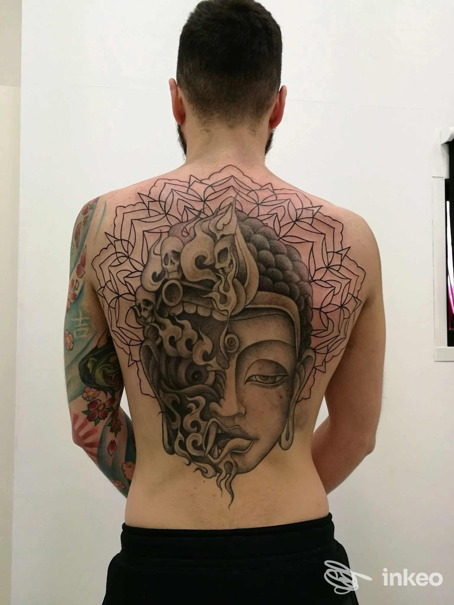 Ampio tatuaggio black & grey su schiena di una persona, opera centrale a volto ornamentale. Love Hate Tattoo, Roma.