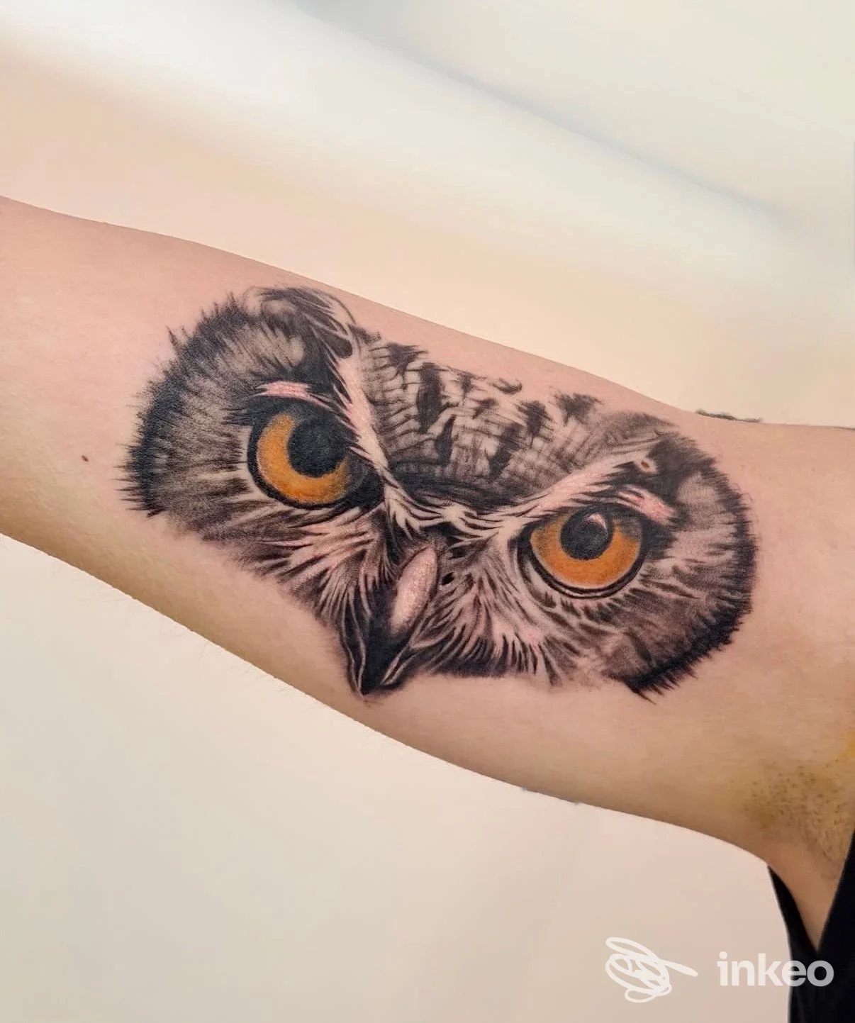 Tatuaggio realistico e dettagliato di un gufo sull'avambraccio, eseguito da Mad Whale Tattoo Studio a Roma, con occhi giallo-arancio intensi.