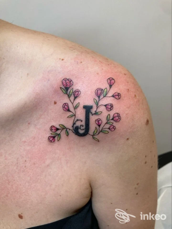 Tatuaggio a forma di lettera 'J' con piccoli fiori rosa sulla spalla, Old Store Tattoo, Roma.