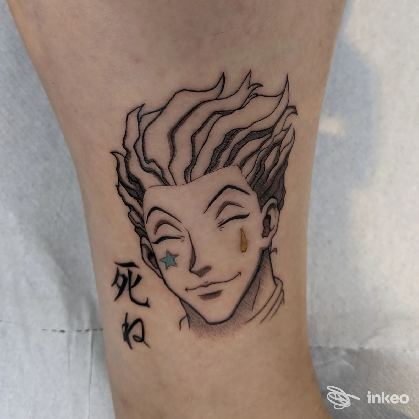 Tatuaggio su gamba: volto stilizzato con stellina blu e lacrima gialla, SHARINK • Tattoo & Piercing a Latina.