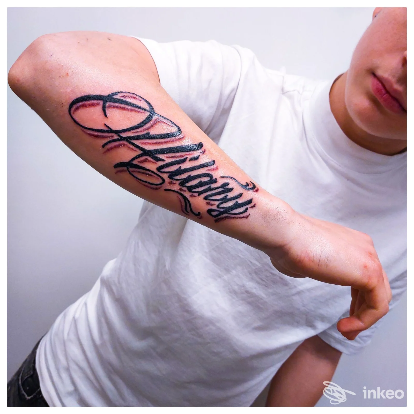 Tatuaggio calligrafico nero sull'avambraccio, foto inviata da Rated R Tattoo Roma, Roma; inquadratura mostra anche parte del volto in dettaglio.