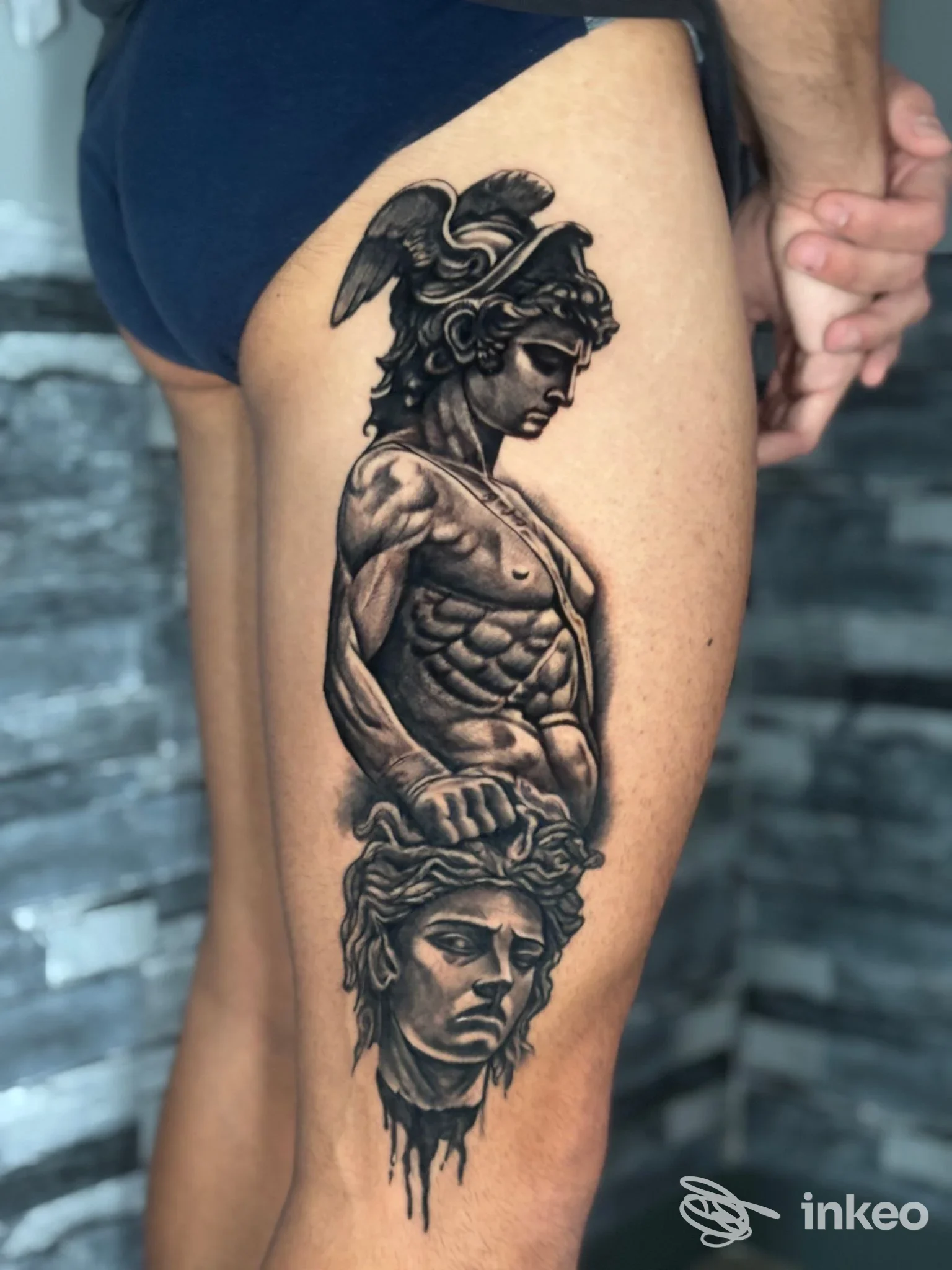 Tatuaggio realistico in bianco e nero su coscia, ritraente un guerriero con elmo e una testa sottostante. T'n'T Ink tattoo studio, Nepi.