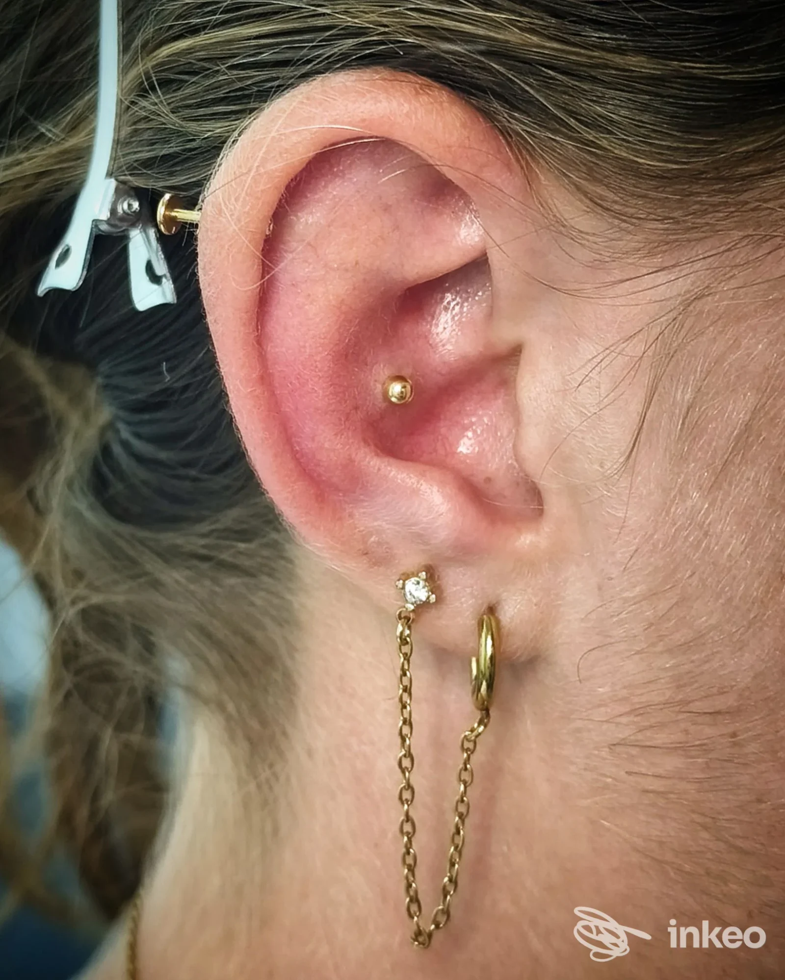 Primo piano di un orecchio con più piercing in oro e una catenella decorativa, foto da studio a Roma.