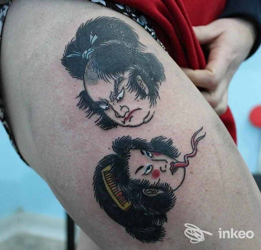 Due volti stilizzati tatuati sulla coscia di una persona, nero e rosso predominanti. Seahorse Tattoo, Roma.