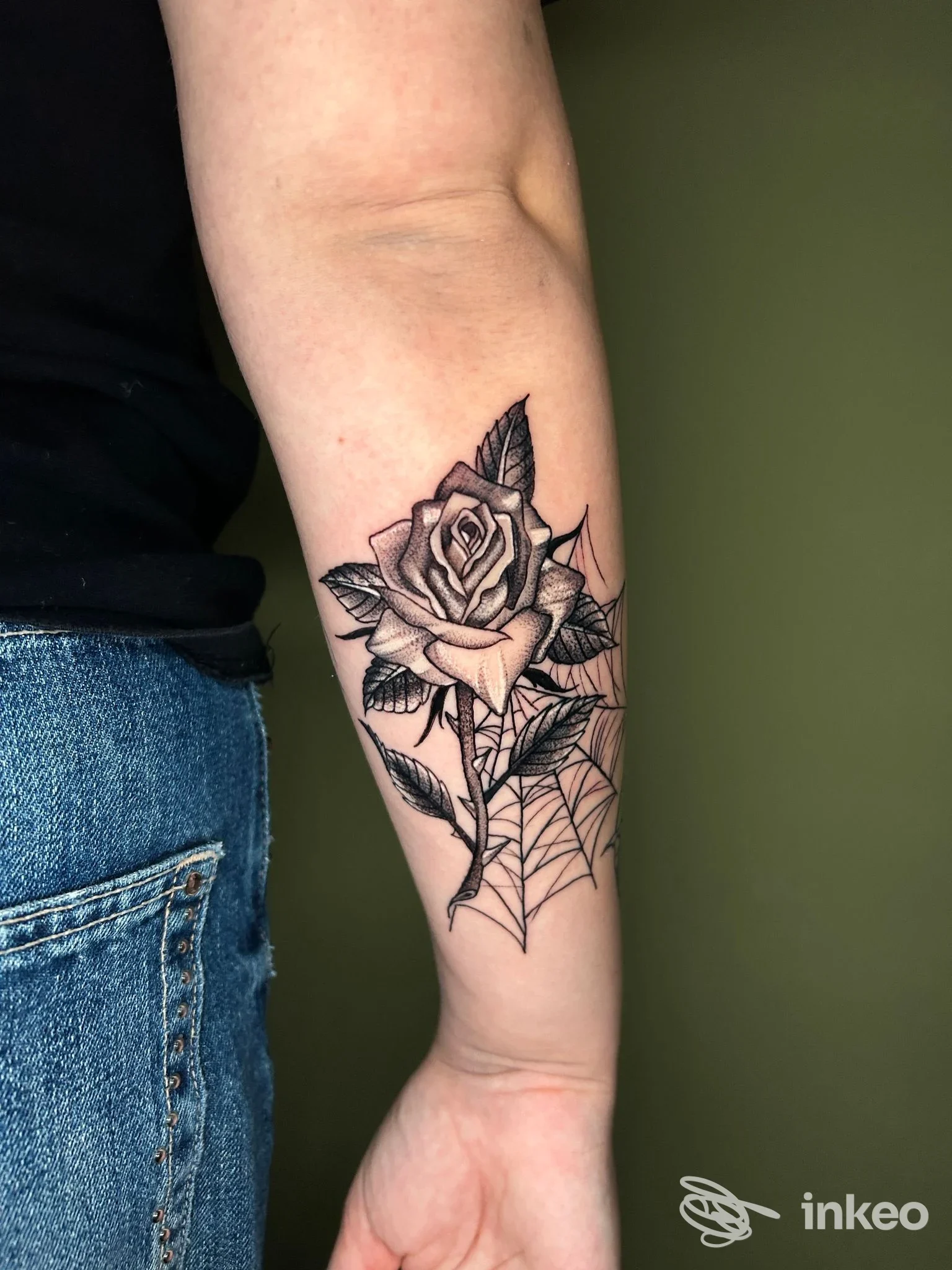 Tatuaggio a inchiostro nero di una rosa con ragnatela sul lato interno dell'avambraccio, fotografato per Sigillum Tattoo Shop & Piercing, Roma.