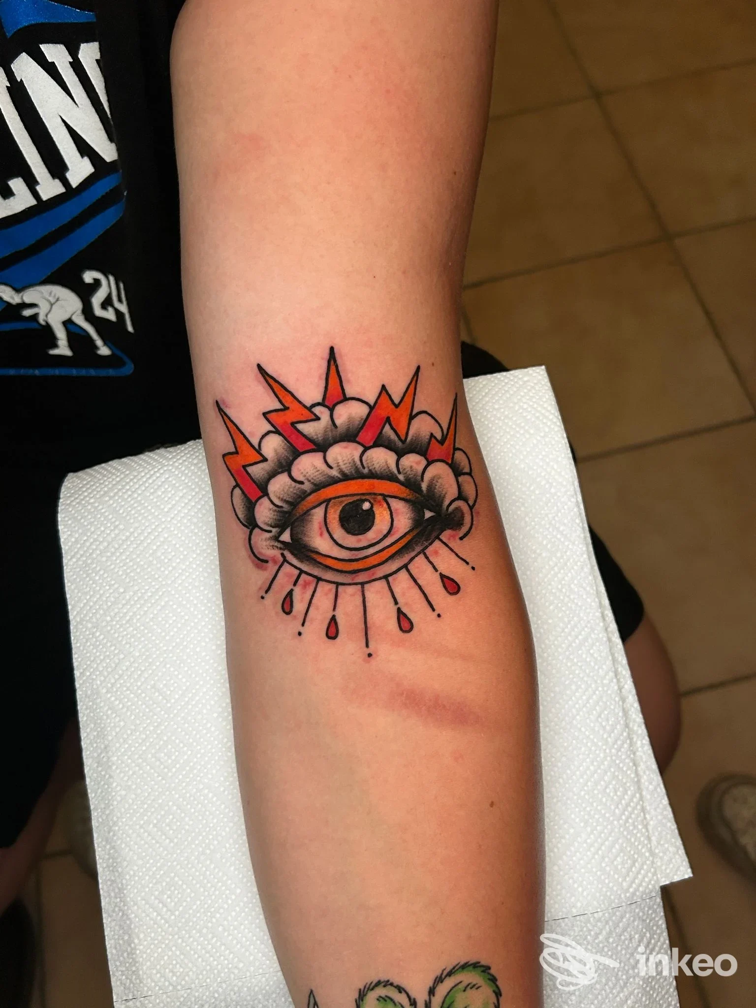 Tatuaggio a Roma presso Sigillum tattoo shop & piercing: occhio stilizzato colorato sull'avambraccio fotografato su tovagliolo bianco.