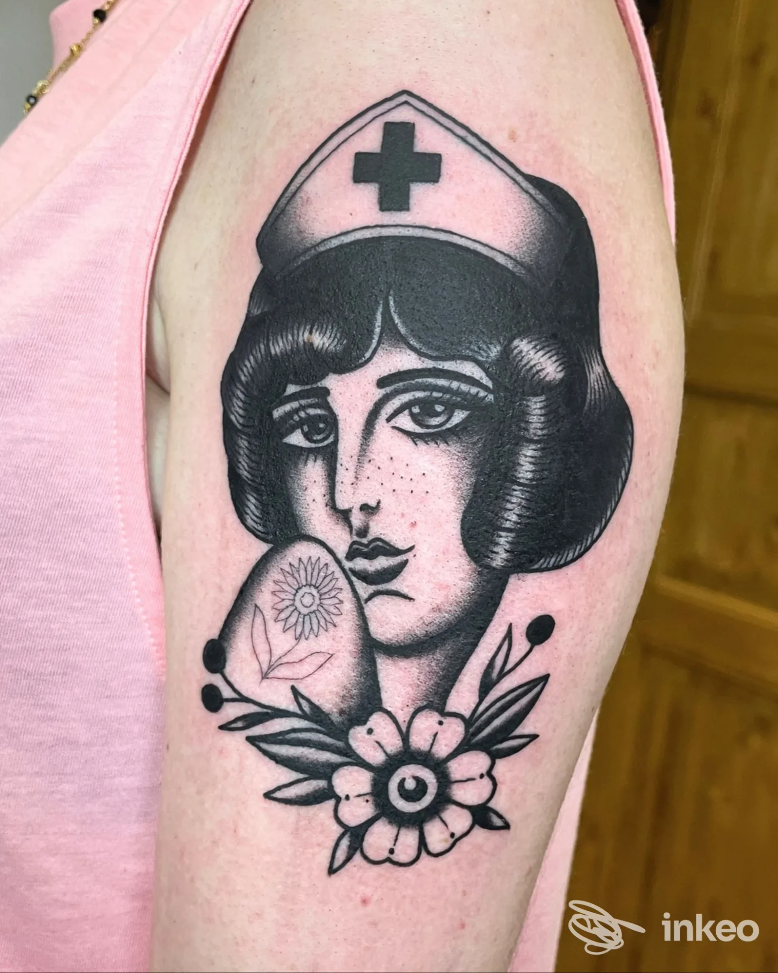 Foto di un tatuaggio sul braccio superiore: volto di un'infermiera in stile tradizionale con fiore, The Shelter Tattoo Studio, Montalto di Castro.
