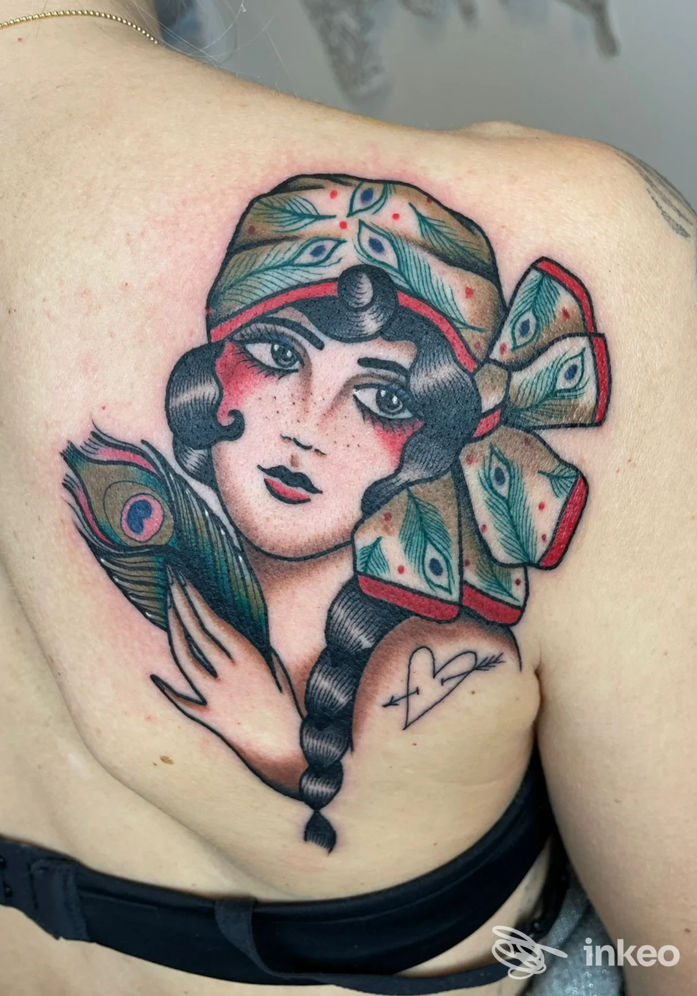 Grande tatuaggio di una donna con foulard e piume sulla spalla superiore, The Shelter Tattoo Studio, Montalto di Castro.