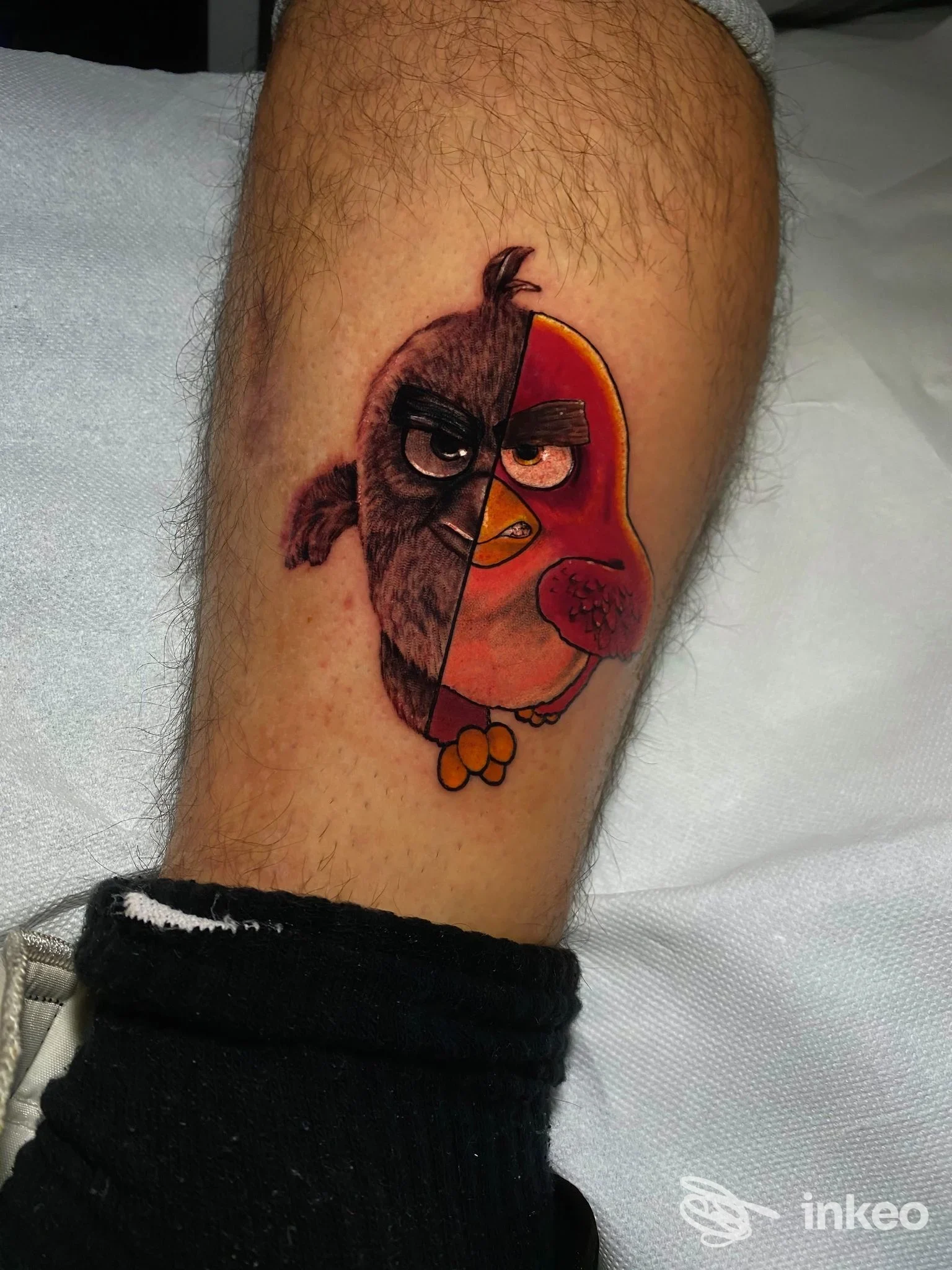 Tatuaggio a colori su polpaccio raffigurante un uccellino in due metà, scatto fornito da Thunder Ink Tattoo, Roma.