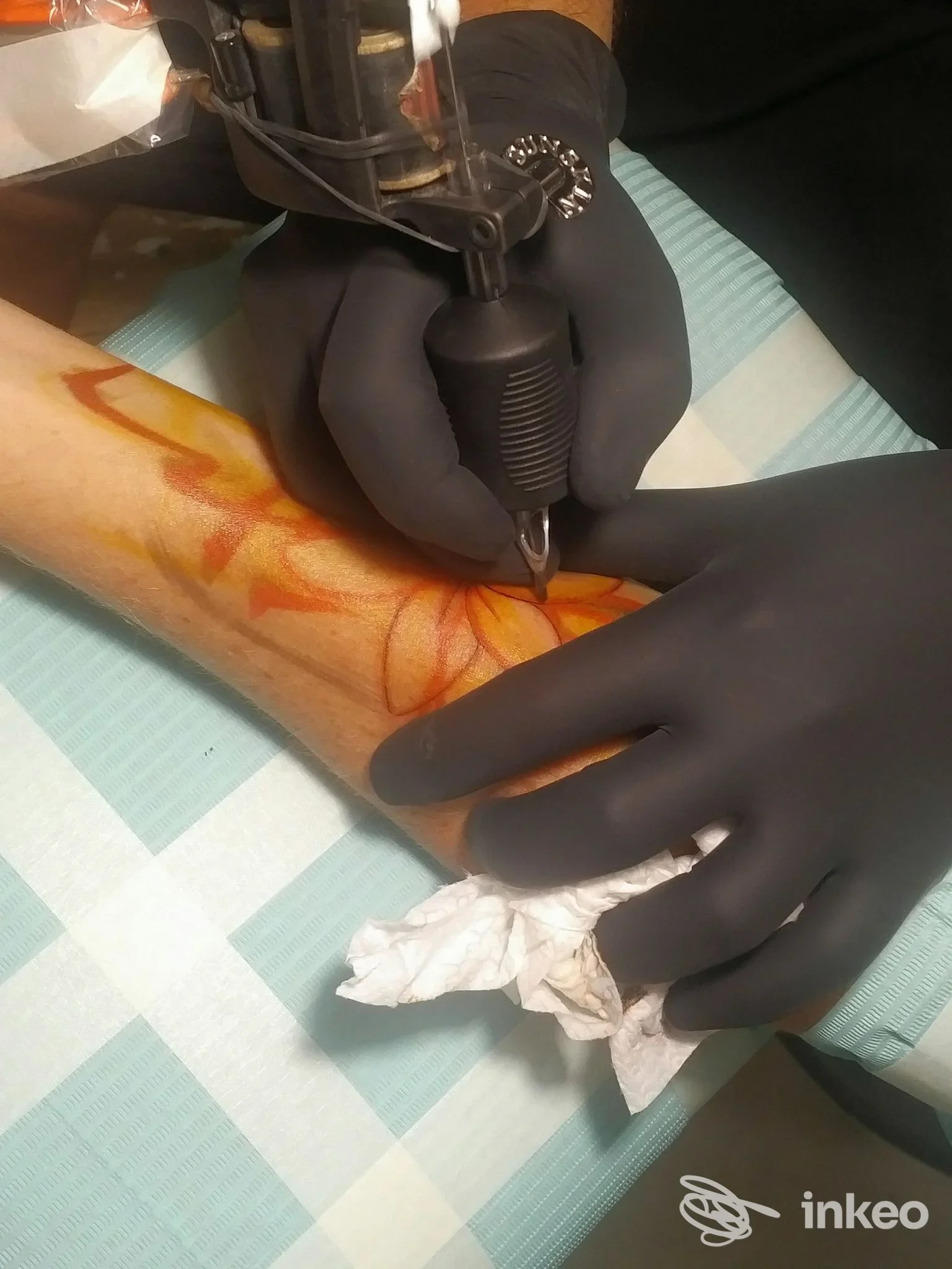 Tatuaggio in corso su avambraccio eseguito presso Unopercento Tattoo Studio, Roma; mani guantate e macchina per tatuaggi in azione.