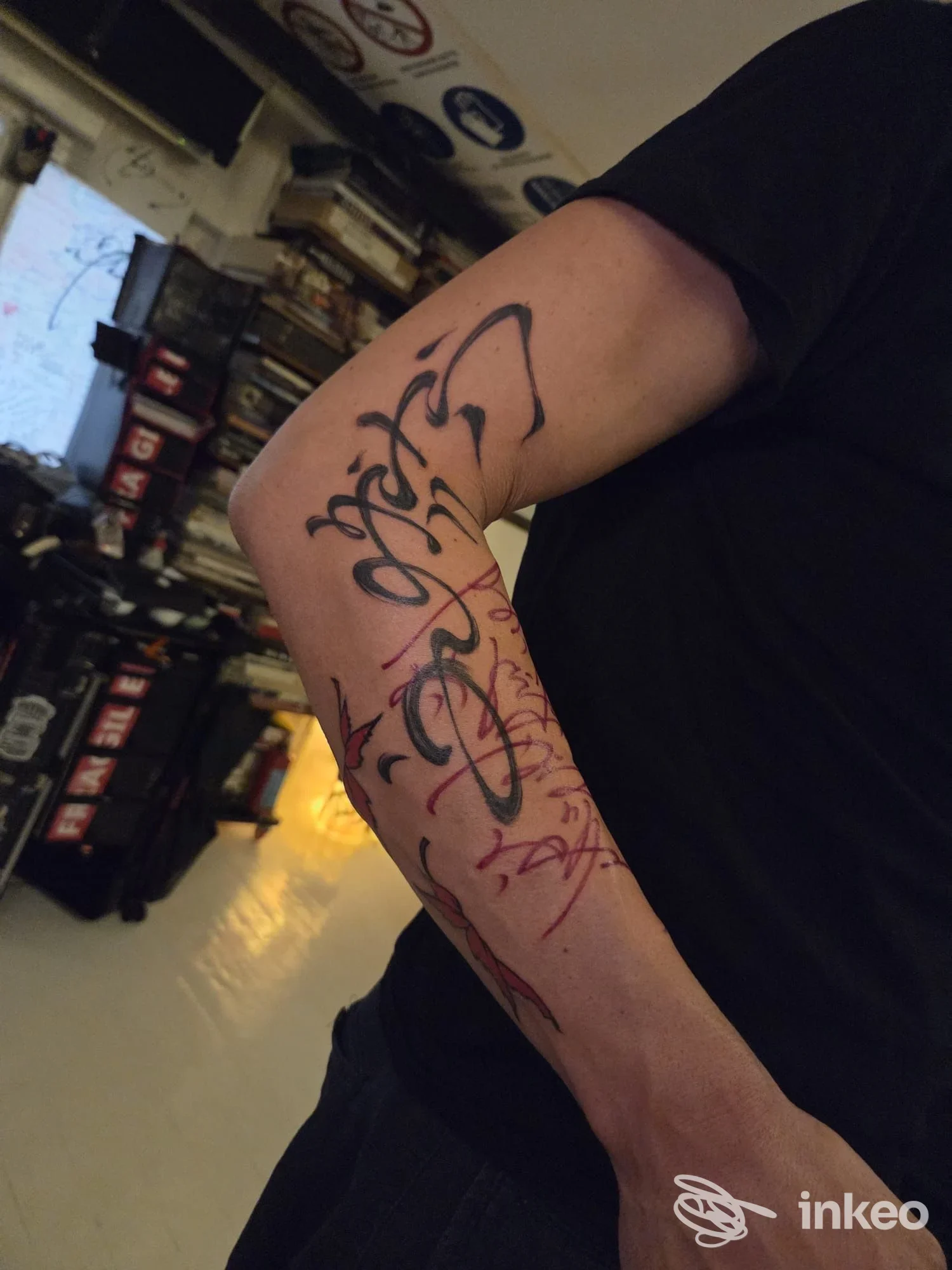 Avambraccio con tatuaggio calligrafico in nero e segni rossi, fotografia da Unopercento Tattoo Studio, Roma.