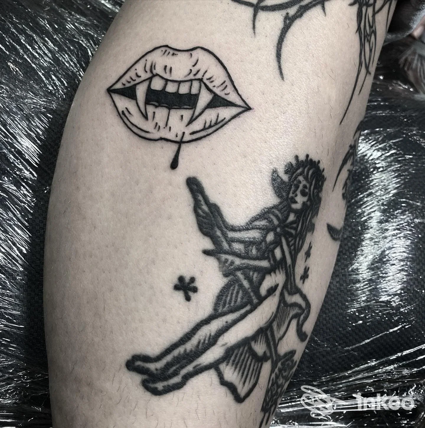 Dettaglio di tatuaggi in bianco e nero sul polpaccio, bocca con zanne e figura stilizzata. Foto di Yama Tattoo, Roma.