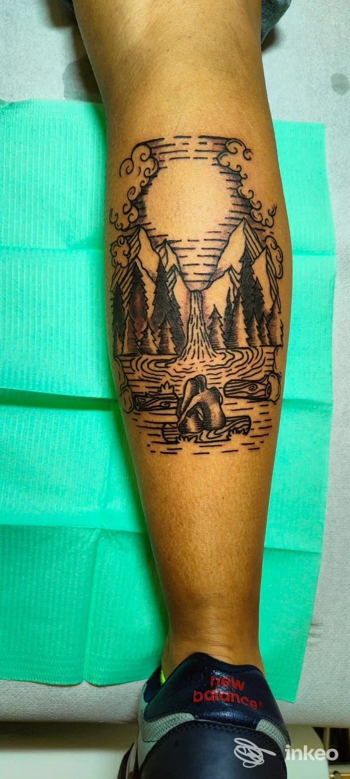 Tatuaggio blackwork/linee su polpaccio: paesaggio con montagne, alberi e lago. Opera pubblicata da Anima Alchemica, Fiumicino.