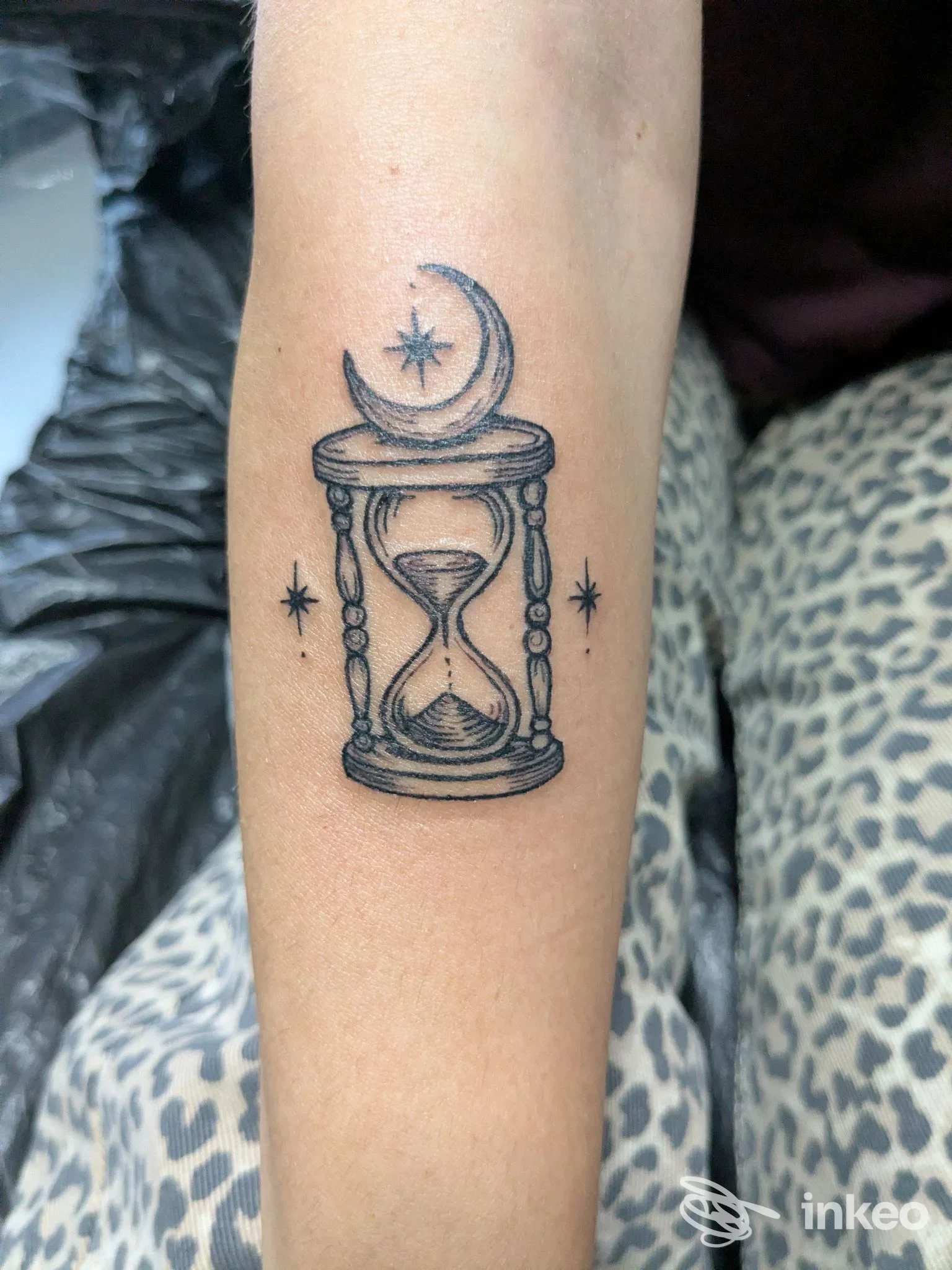 Tatuaggio su avambraccio: clessidra con luna crescente e stelle, eseguito da Alles Tattoo & Piercing Studio, Roma.