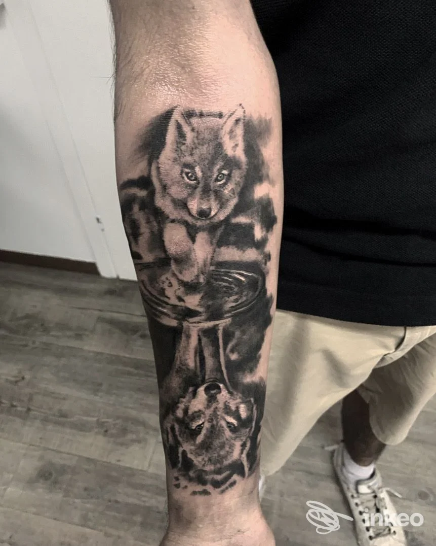 Fotografia di un tatuaggio realistico in bianco e nero sull’avambraccio: due volpi, una in alto e una in basso, raffigurate con sfumature di grigio.