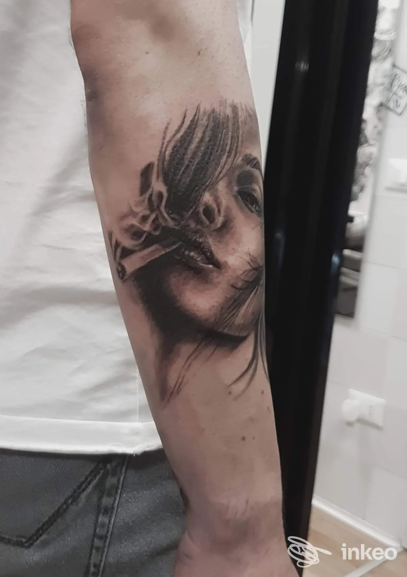 Primo piano di un tatuaggio realistico in bianco e nero, volto di donna che fuma sull'avambraccio. Beautiful Ink, Roma.