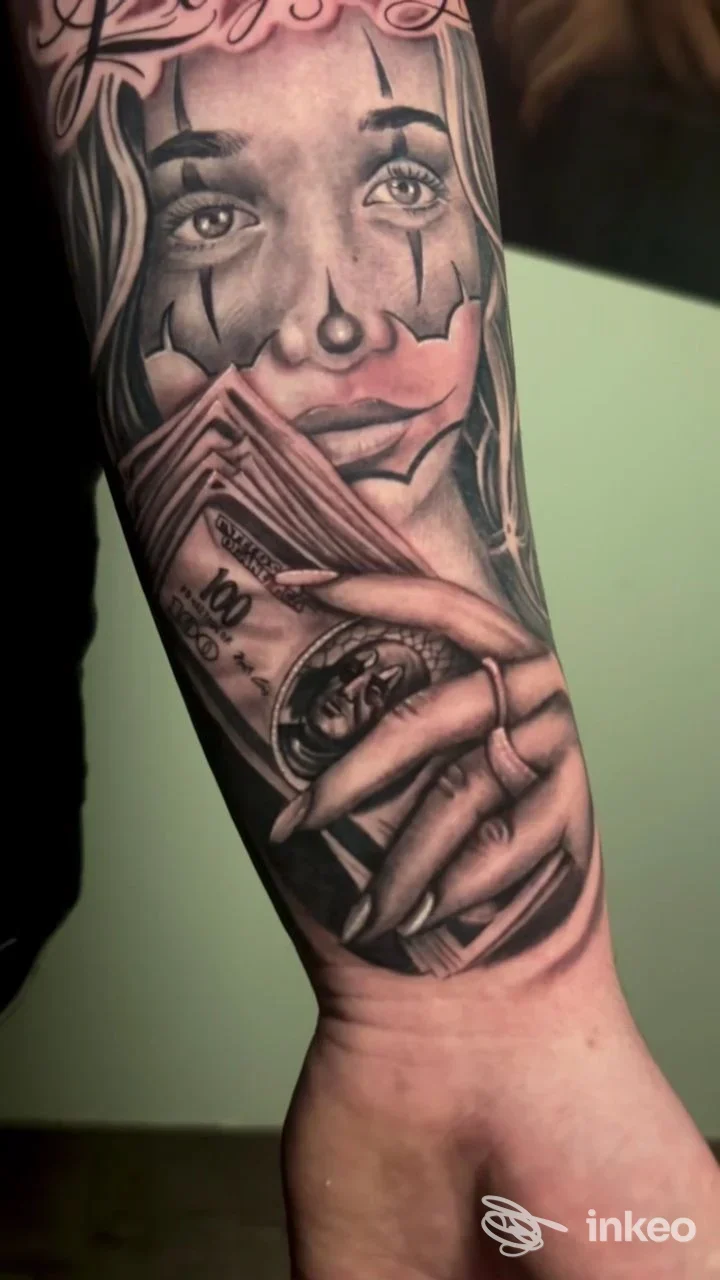 Tatuaggio in bianco e nero su avambraccio raffigurante volto di clown e mano che tiene una banconota. Arte su pelle, Formia.
