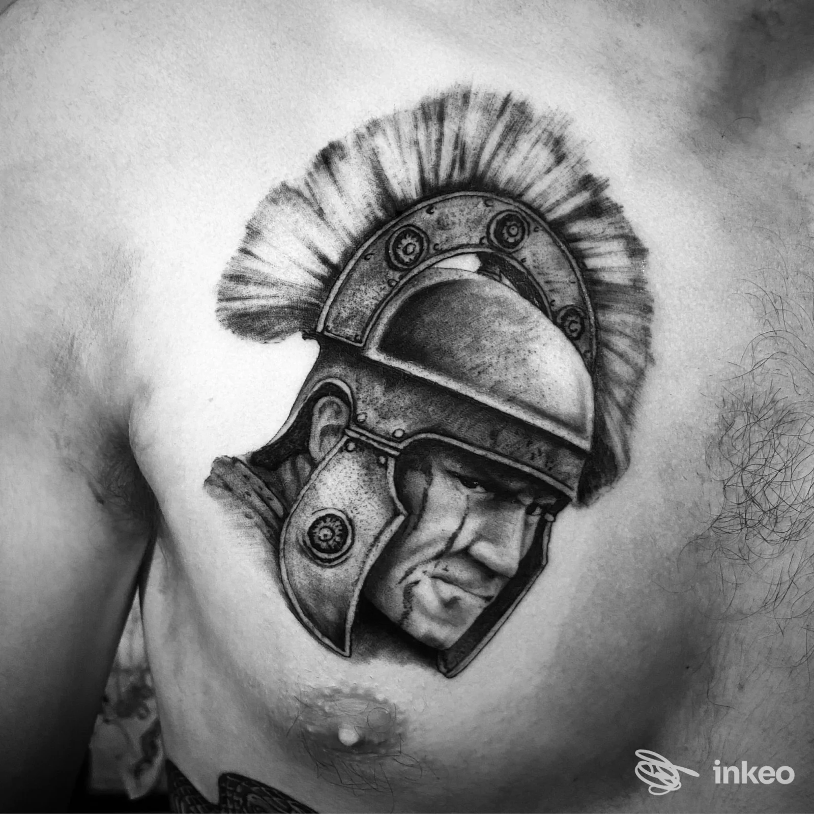 Tatuaggio realistico in bianco e nero sul petto raffigurante un elmo romano con volto, realizzato da Bent Back Studios, Roma.